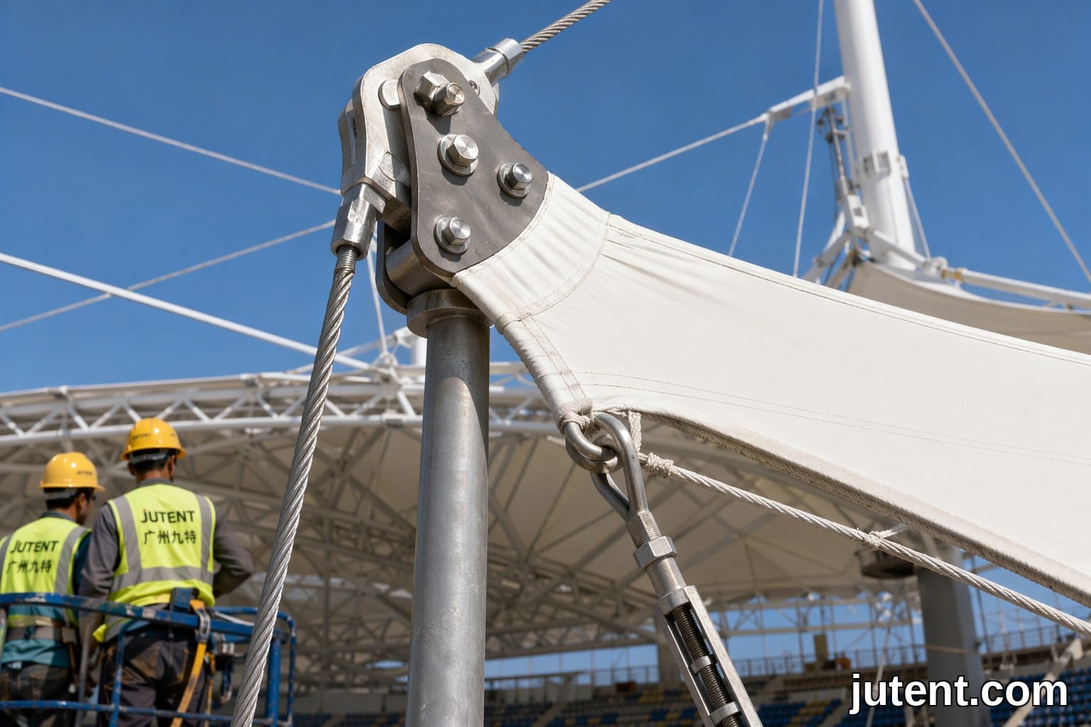 Primer plano de la parte superior del mástil de acero con cable de cumbrera y abrazadera de membrana en una cubierta tensada de Jutent para cumplimiento de carga de viento en anfiteatro