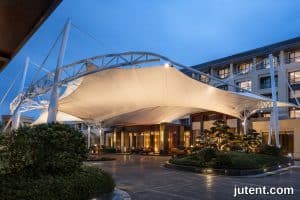 Modern hotel tensile canopy structure with curved membrane providing shade and UV protection for outdoor guest area