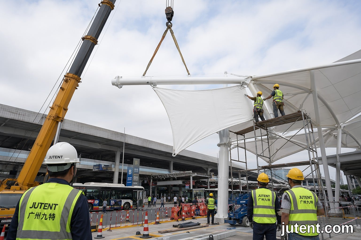 Trabajadores de construcción instalando un toldo de membrana tensada prefabricado en una terminal de tránsito activa utilizando una grúa.