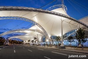 Struktur kanopi membran tegangan terminal transit moden di stesen bas yang sibuk dengan kenderaan berkelegaan tinggi di bawahnya