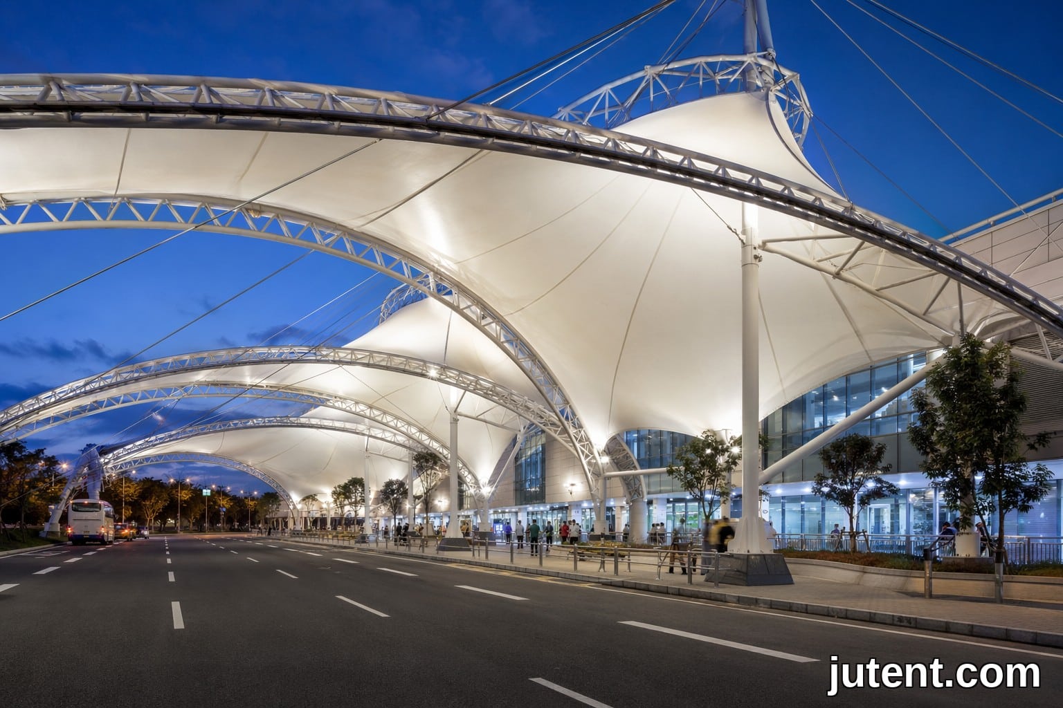 Modern transit terminal tensile membrane canopy structure at a busy bus station with high-clearance vehicles underneath