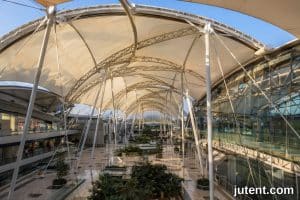 Estrutura moderna de cobertura de átrio em membrana tênsil no interior de edifício comercial com luz natural, comparando benefícios de custo em relação ao vidro
