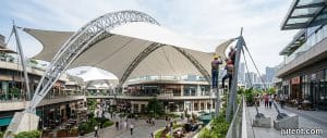 Modern tensile membrane canopy shading a retail walkway in Dubai with intense sunlight and heat haze visible