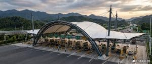 Highway toll station canopy with tensile membrane structure spanning multiple lanes, showcasing anti-corrosion steel frame and wind-resistant design