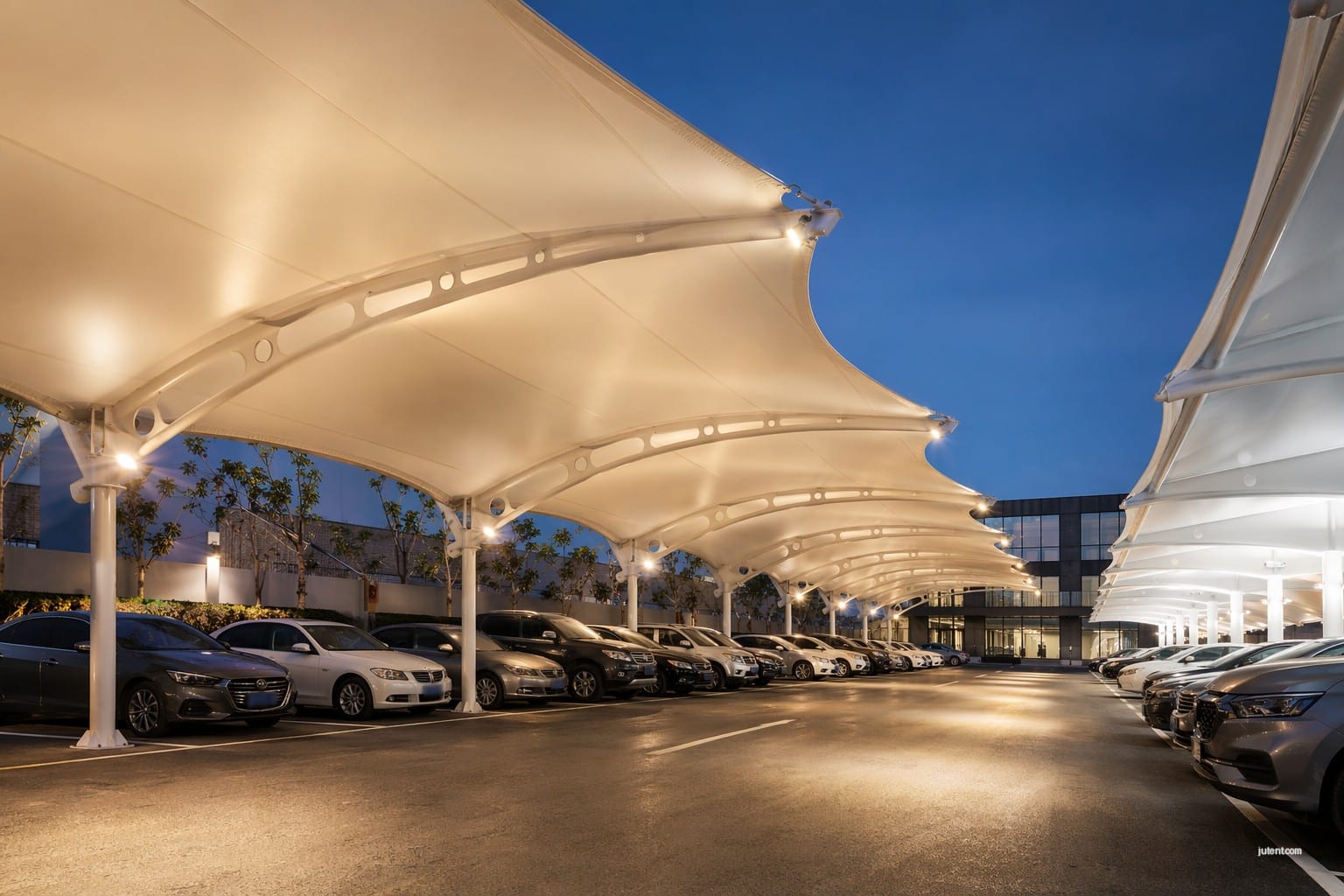Large white tensile membrane parking canopy installed over vehicles, showcasing modern commercial shade structure alternative to standard steel