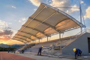 Grande structure d'ombrage modulaire pour gradins avec toiture en membrane tendue recouvrant les sièges du stade sous une lumière solaire éclatante
