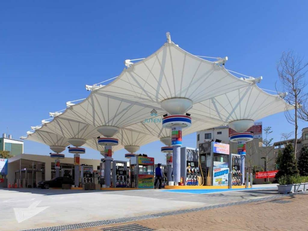 Commercial gas station canopy with inverted umbrella tensile membrane providing full coverage for the fueling area.