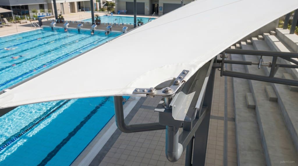 Close architectural detail of chlorine-resistant membrane and steel connection in a pool tensile shade structure